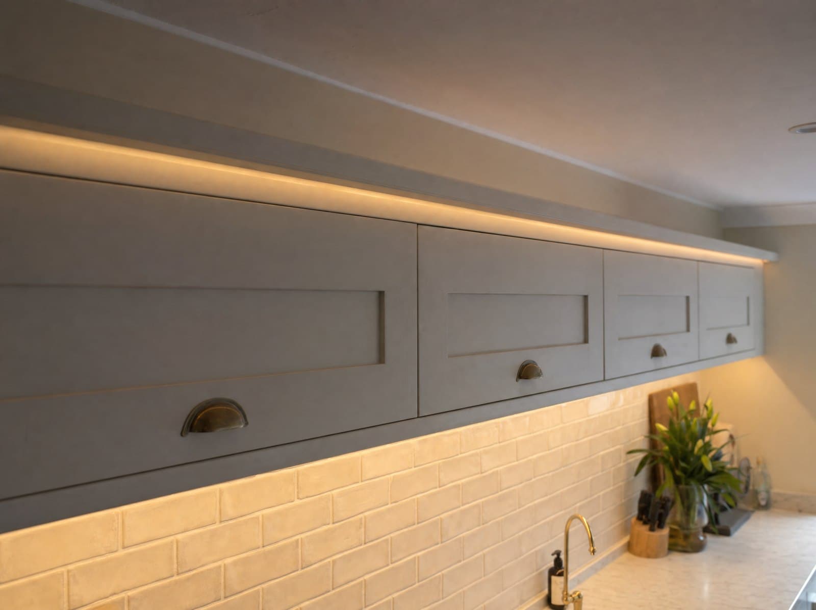 AI-generated illustration: a painted cabinet pelmet running above wall units with warm 2700K LED light spilling onto the worktop below, used as a pelmet reference.